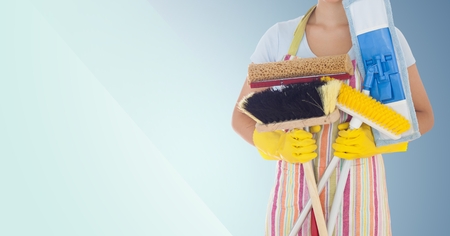 Mid-section of female cleaner holding brushes against blue backgroundの写真素材