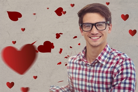 Portrait of smiling nerd man in spectacles against digitally generated red heartsの写真素材
