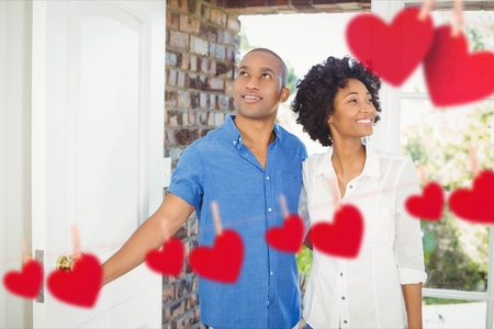 Composite image of red hanging hearts and happy couple entering homeの写真素材
