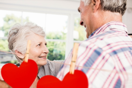 Composite image of red hanging hearts and happy senior couple dancing at homeの写真素材