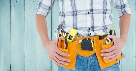 Mid section of handyman with tool belt against wooden backgroundの写真素材