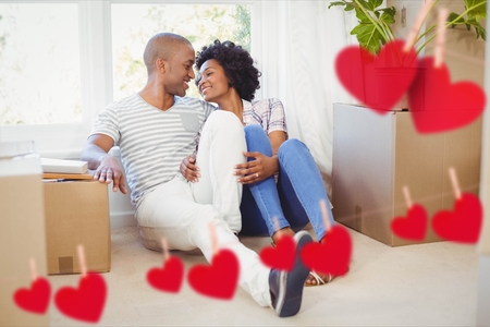 Romantic couple embracing in living room at home against hearts hanging on a lineの写真素材