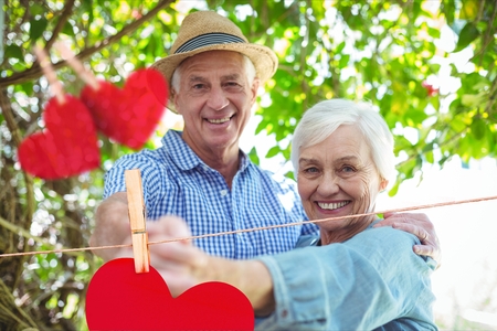 Composite image of red hanging hearts and smiling senior couple dancing outdoorsの写真素材