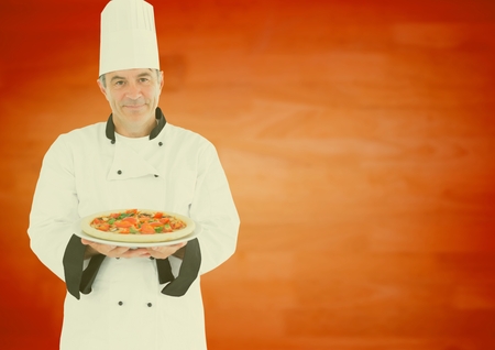 Portrait of smiling male chef presenting food against orange backgroundの写真素材
