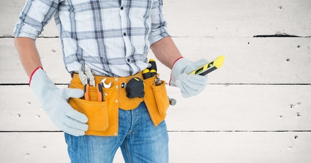 Mid section of handy mans torso with tool belt against wooden panelの写真素材