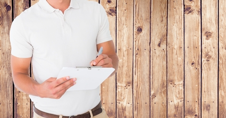 Mid section of delivery man writing on clipboard against wooden backgroundの写真素材