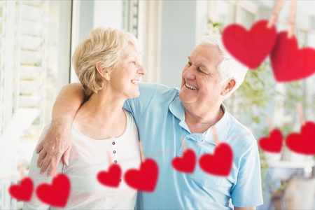 Composite image of red hanging hearts and smiling senior couple embracing outdoorsの写真素材