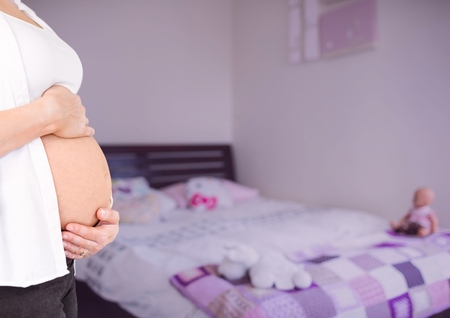 Digital composite of Pregnant woman mid section holding stomach in blurry bedroom with pink overlayの写真素材