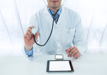 Digital composite of Doctor with stethoscope and devices at desk against blurry windowの写真素材