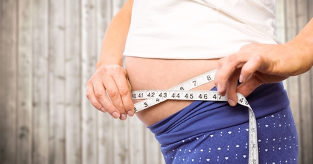 Digital composite of Pregnant woman mid section with measuring tape against blurry wood panelの写真素材