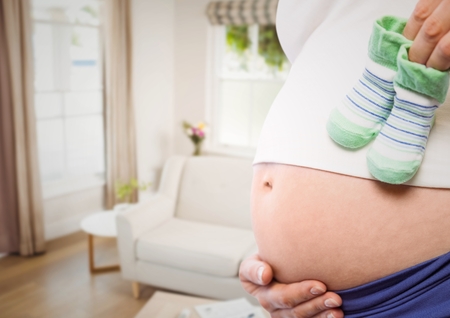 Digital composite of Pregnant woman mid section holding socks against blurry sitting roomの写真素材
