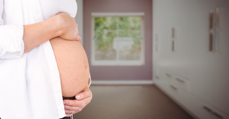 Digital composite of Pregnant woman mid section holding stomach in blurry hallwayの写真素材