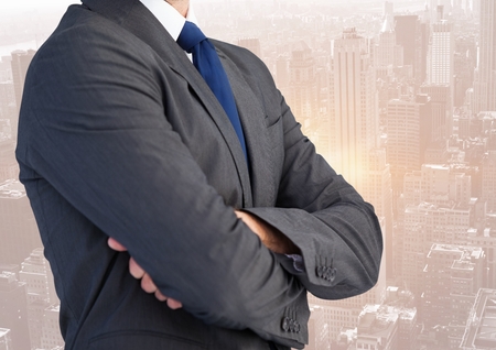 Digital composite of Business man mid section with arms folded against skylineの写真素材