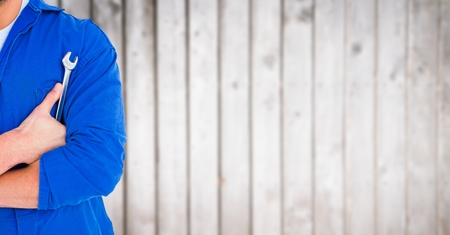 Digital composite of Mechanic with arms folded and wrench against blurry wood panelの写真素材