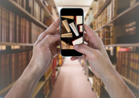 Digital composite of Hand with phone showing standing books against blurry bookshelvesの写真素材