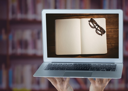 Digital composite of Hands with laptop showing open book and glasses against blurry bookshelf with purple overlayの写真素材