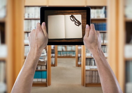 Digital composite of Hands with tablet showing open book and glasses against blurry archwaysの写真素材