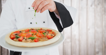 Digital composite of Chef putting herbs on pizza against blurry wood panelの写真素材