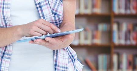 Digital composite of Womans hands touching tablet in Libraryの写真素材