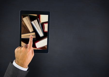 Digital composite of Hand touching tablet showing standing books on navy tableの写真素材