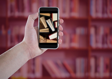 Digital composite of Hand with phone showing standing books against blurry bookshelf with red overlayの写真素材