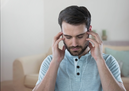 Digital composite of Stressed man on headphones relaxing at homeの写真素材