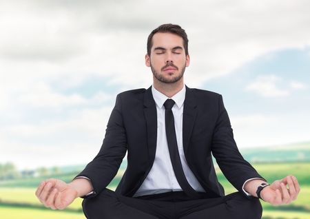 Digital composite of Businessman Meditating by green fieldsの写真素材