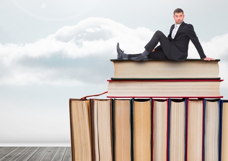 Digital composite of Man sitting on Books stacked by cloudy skyの写真素材