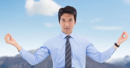 Digital composite of Businessman Meditating against blue sky mountainの写真素材