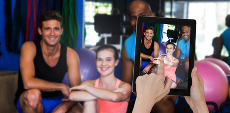Hands touching digital tablet against white background against portrait of happy friendsの写真素材