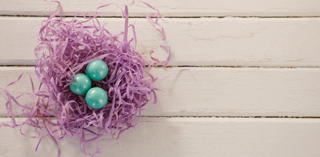 Overhead shot of turquoise Easter eggs in violet nest on wooden table