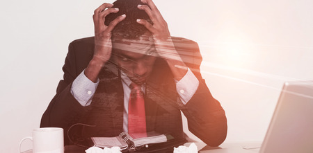 Light trails on city street against frustrated afro businessman with head in hands at deskの写真素材