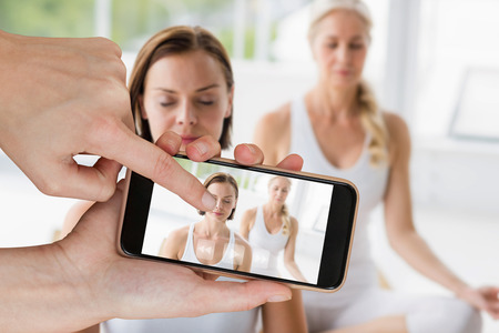 Hands touching smart phone against women with eyes closed doing yogaの写真素材