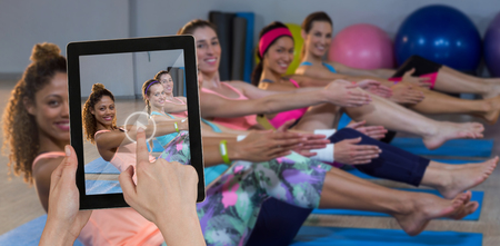 Hands touching digital tablet against white background against portrait of women performing yogaの写真素材