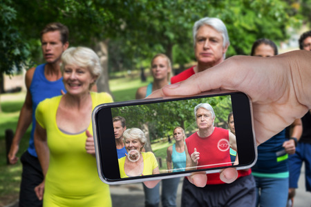 Hand holding mobile phone against white background against marathon male and female athletes runningの写真素材