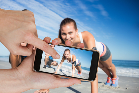 Hands touching smart phone against portrait of couple exercising on sandの写真素材