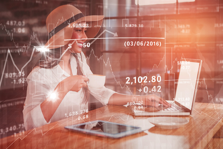 Stocks and shares against woman having coffee while using laptop in cafeの写真素材