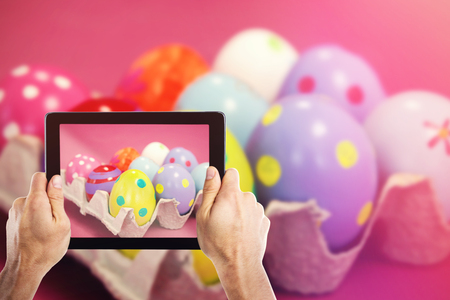Cropped hand holding digital tablet against colorful easter eggs in egg cartonの写真素材