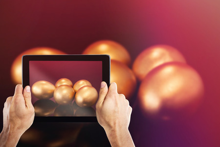 Cropped hand holding digital tablet against golden easter eggs on colored backgroundの写真素材