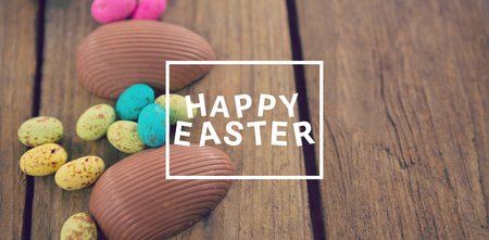 Easter greeting against chocolate easter eggs on wooden plankの写真素材
