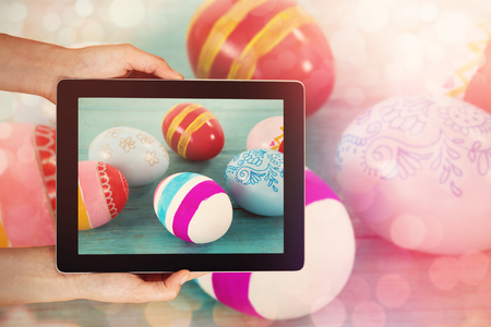 Close-up of hands holding digital tablet against various easter eggs on wooden surfaceの写真素材
