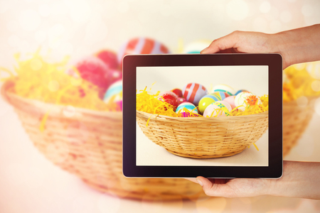 Close-up of hands holding digital tablet against painted easter eggs in basketの写真素材