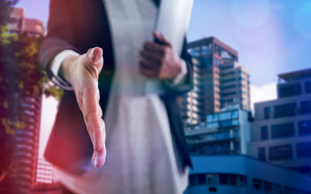 Corporate woman offering handshake against beautiful cityscape against clear skyの写真素材