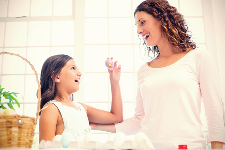Happy girl showing easter egg to her mother in the living roomの写真素材