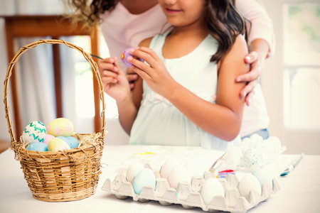Happy mother and daughter painting easter eggs in the living roomの写真素材