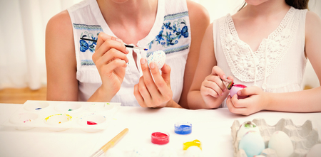 Mother and daughter painting easter eggs at home in the living roomの写真素材