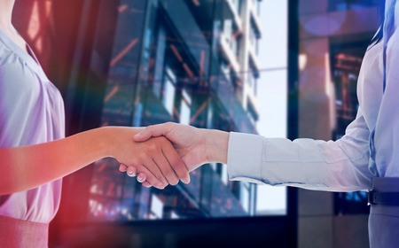 Businesswomen shaking hands against exterior of modern buildingの写真素材
