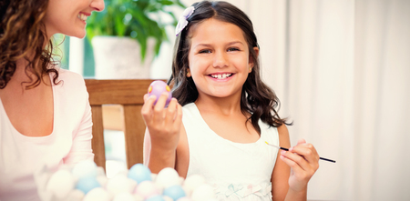 Happy mother and daughter painting easter eggs in the living roomの写真素材