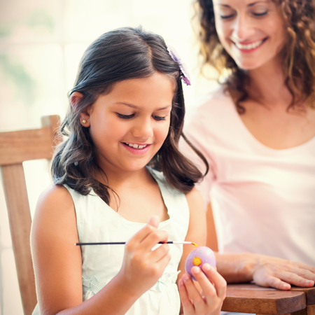 Happy mother and daughter painting easter eggs in the living roomの写真素材