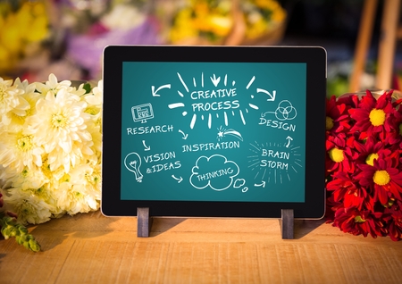 Digital composite of Tablet on florist table showing white design doodles against teal backgroundの写真素材